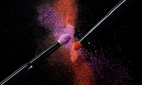 two eye shadow brushes with bright purple and red eyeshadow powder on black background