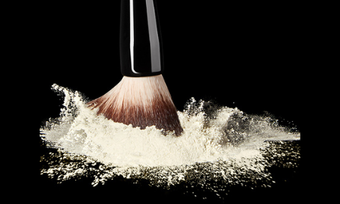 Powder makeup brush in light translucent loose setting powder on black background