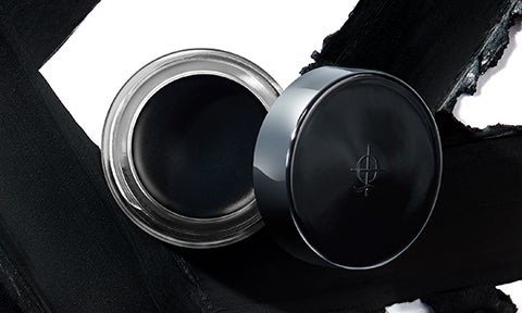 Illamasqua black gel eyeliner pot with open lid in front of streaks of black gel eyeliner on background