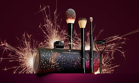 Makeup brush kit with powder brushes, eyeshadow brush and eyelash curlers in front of sparklers