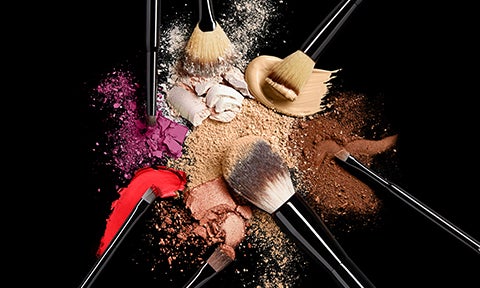 powder, foundation, fan and concealer makeup brushes with crushed makeup products in background