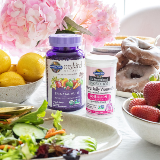 Mykind Organics Prenatal multivitamins and Dr Formulated Probiotics Once Daily Women's standing on the table surrounded by berries, salad and donuts