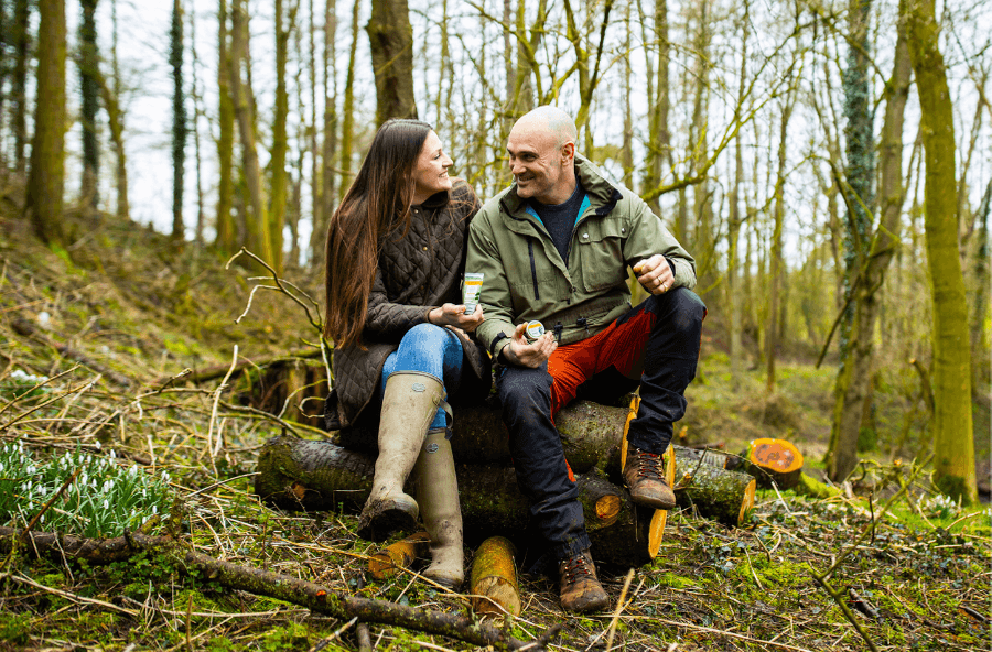 Ed and Laura sat on a log outside holding tins of the Burt's Bees Res Q Cream and Ointment with Cica