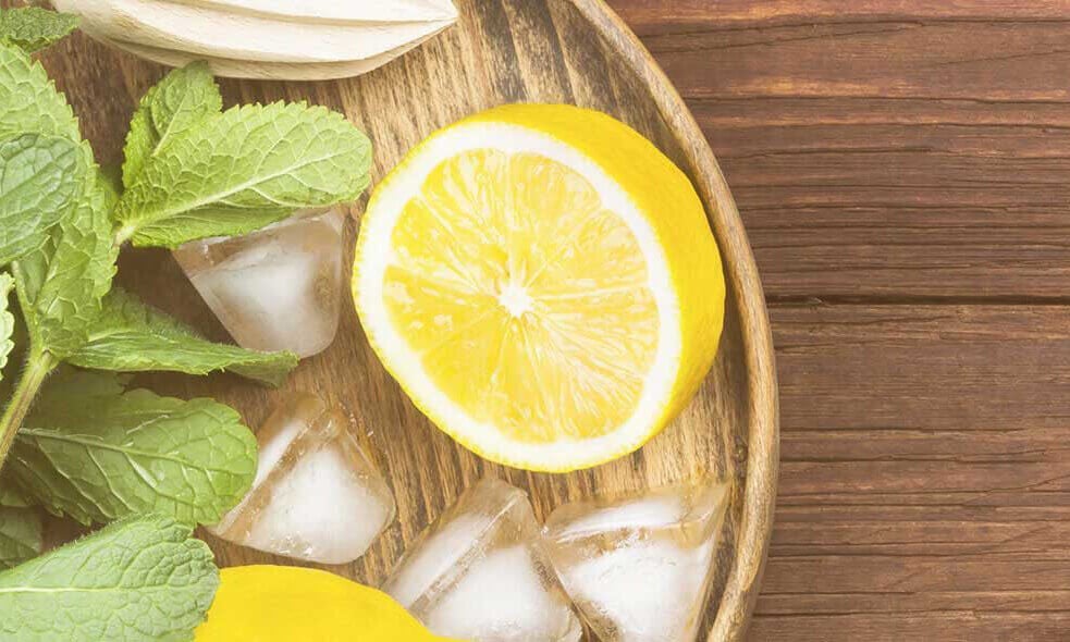 Half a lemon on a wooden tray next to mint leaves and ice cubes
