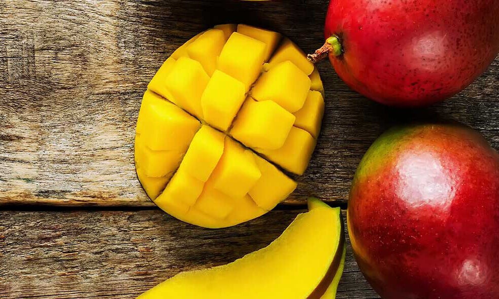 A sliced up mango next to whole mangoes