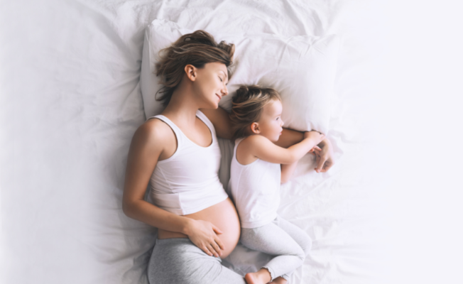 A pregnant woman cuddling with her toddler.
