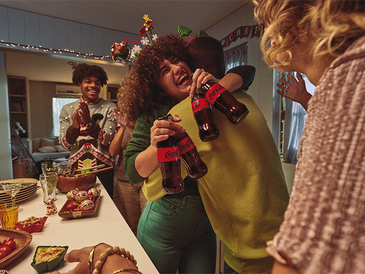 friends hugging with a Christmas dinner on the table, holding glass bottles of Coca-Cola