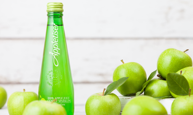 Bottle of Appletiser surrounded by green apples on a white background