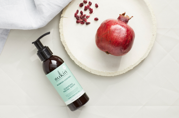 Sukin Blemish control cleansing facial wash next to a plate with a pomegranate on it.
