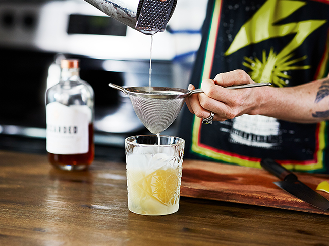 Bartender pouring clear spirit through a strainer into a cocktail