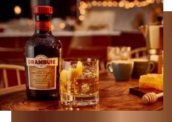 A bottle of Drambuie liqueur with a glass beside it containing a cocktail and ice with orange peel
