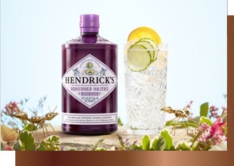 Hendrick's alcohol placed beside a cocktail in a glass, the cocktail contains ice, lemon and lime, the scene is surrounded by wildflowers and a bug