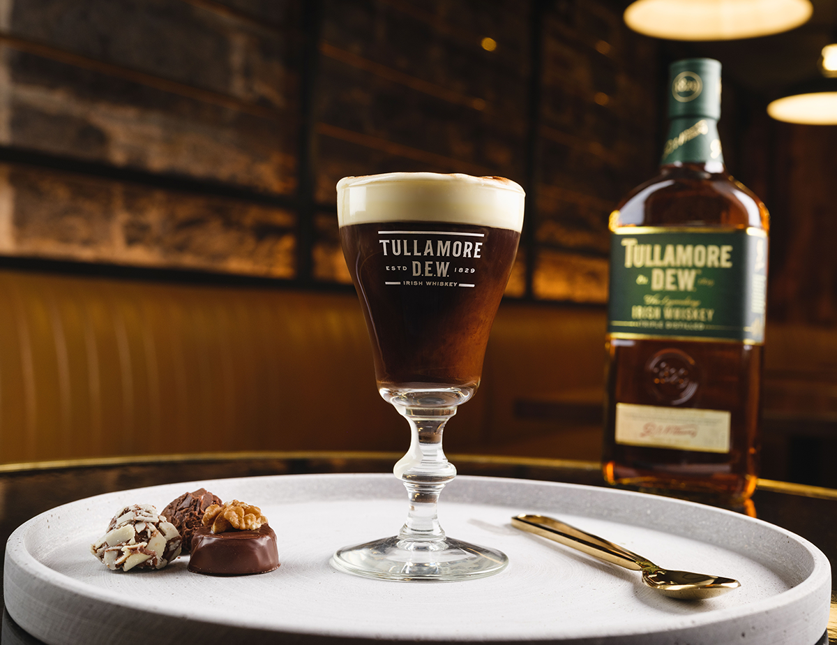 A cocktail with chocolate truffles on the side is present with a bottle of Tullamore D.E.W in the background of the dimly lit brick room