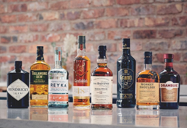 Eight bottles of various gins and whisky's are present with a brick background