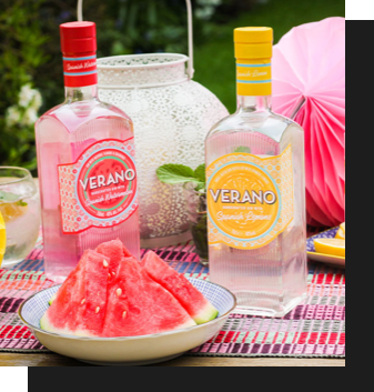 Two bottles of Verano alcohol, one is pink, one is yellow, there is a plate of watermelon in the foreground