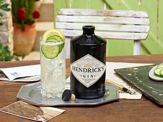Bottle of Hendricks Gin with drink garnished with lemon and cucumber