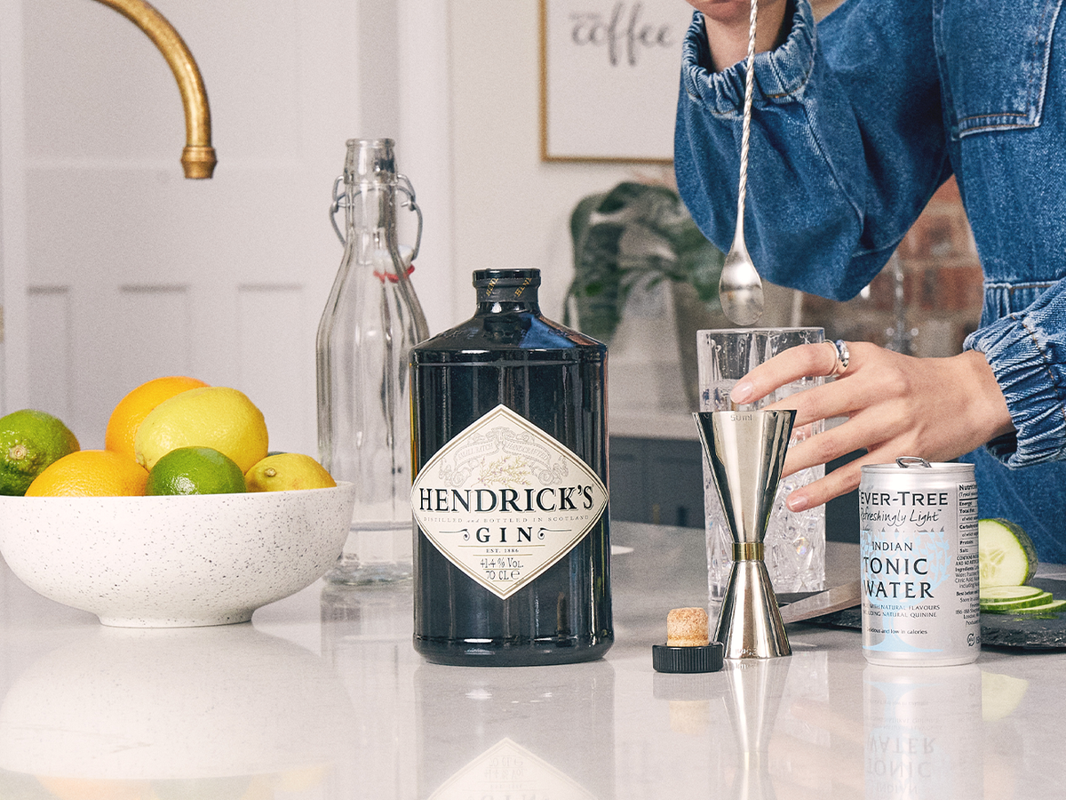 Woman making a drink next to a Hendricks Gin bottle and can of Fever Tree Tonic Water