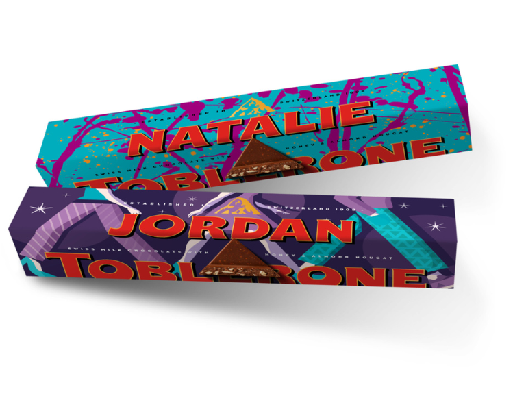 1 Blue Packaged Personalised Toblerone Bar reading 'Natalie' and 1 Purple packahed Personalised Toblerone Bar reading 'Jordan', sitting next to eachother, in front of a white back ground.