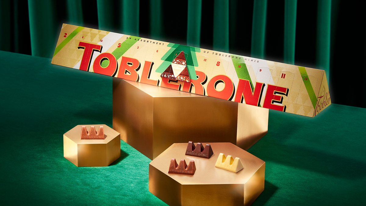 Triangle of Toblerone posing as a superhero in front of a green curtain with mini chocolates of Toblerone next to it