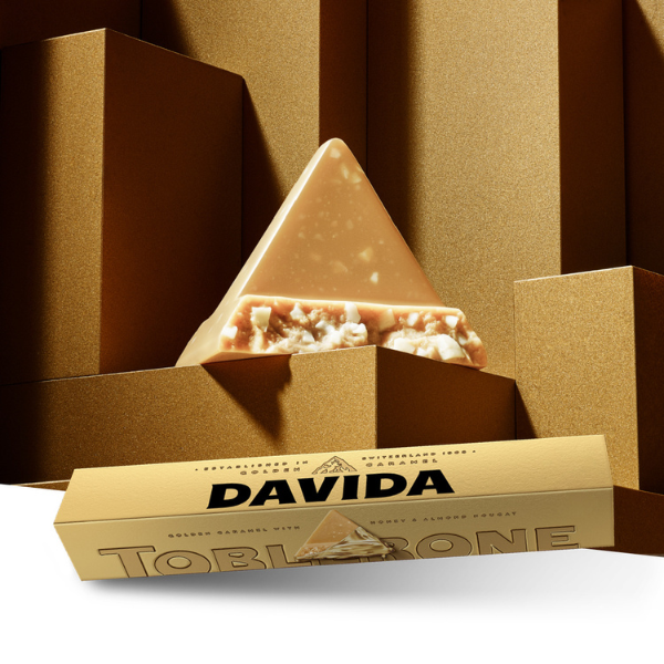 Personalised Toblerone Gold Bar with the name Davida printed on the packaging. Situated in front a traingle shaped chocolate piece.