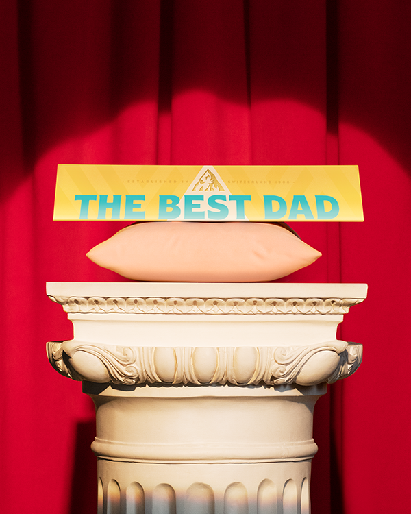 A personalised Toblerone reading 'The Best Dad' on a pillar, in front of a red curtain.