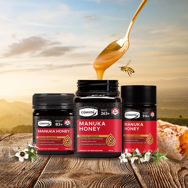 A bundle of manuka honey standing on a wooden table surrounded by nature.