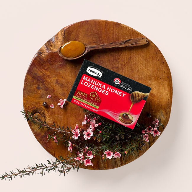 Manuka honey lozenges package laying on a small wooden table. There are flowers and a wooden spoon laying next to the packaging as a decoration. Sign up to get 15% off!