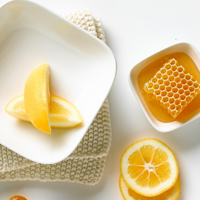 Two plates one with slices of lemon and another one filled with honey standing on a white table. The table is decorated with slices of orange laying next to plates.