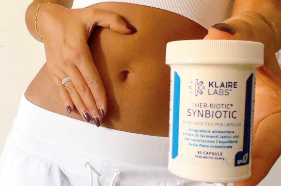 Una donna con una bottiglia di Ther-biotic Synbiotic del Klaire Labs in mano e l'altra mano sulla sua pancia