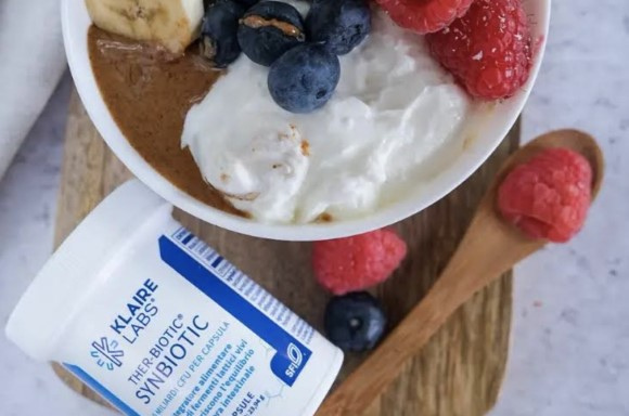 Una ciotola di yogurt con vari tipi di bacche sono sul tavolo insieme a un Ther-Biotic synbiotic. I probiotici aiutano a ridurre il dolore e il gonfiore