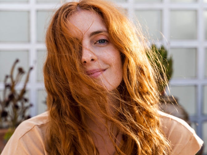 Lady with ginger hair, smiling at the camera with her hair over one eye