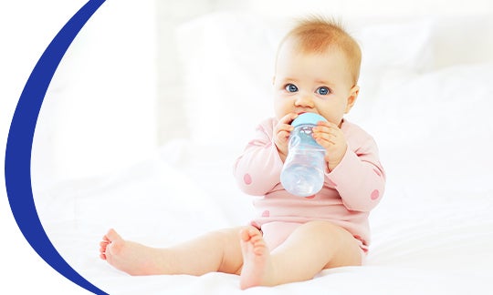 Dziecko siedzące na łóżku i pijące swoje mleko Nestle z butelki.