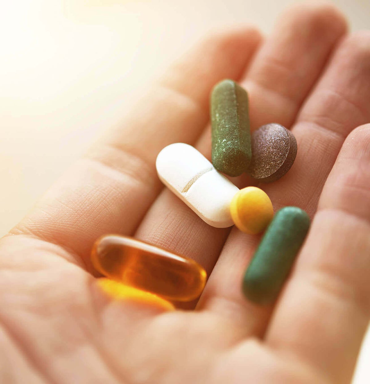 A hand holding various pills of different colours and forms.
