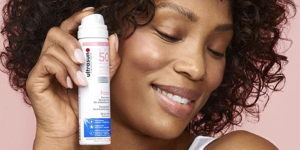 Woman holding Ultrasun UV Face & Scalp Mist SPF50 spray bottle