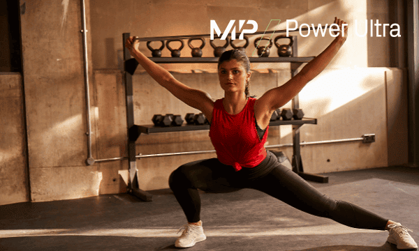 A women working out with weights in a gym in black gym leggings and a red tank crop top.
