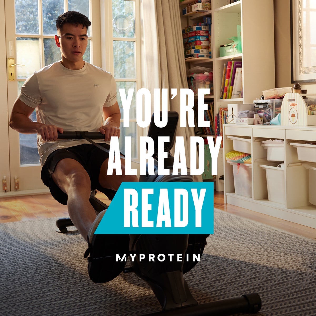A man workout out on a rowing machine at home with the words 'You're Already Ready - MYPROTEIN' overlaying.