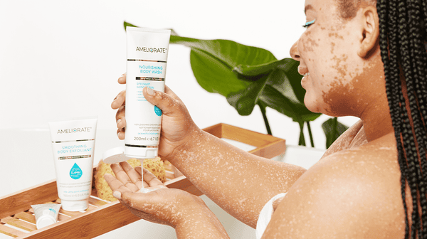 Woman in bath applying Ameliorate nourishing body wash to her skin with Ameliorate smoothing body exfoliant on the bath rack