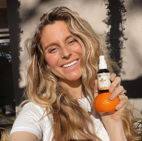 A woman holding a vitamin C spray and smiling