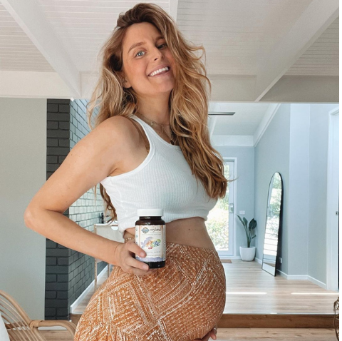A pregnant women holding multivitamins and smiling