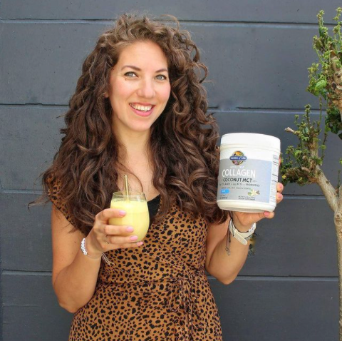 Una giovane donna tiene in una mano una confezione di Collagen coconut MCT e nell'altra un bicchiere contenente una bevanda preparata con lo stesso prodotto.