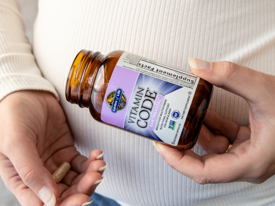 Una donna incinta tiene in mano una confezione di Vitamin Code Raw Integratore prenatale.