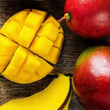 A sliced up mango next to whole mangoes