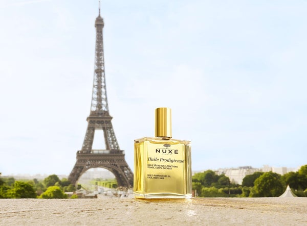 Golden Huile Prodigieuse Bottle in front of the Eiffel Tower