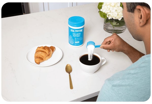 Man sitting at a breakfast bar pouring collagen peptides into coffee