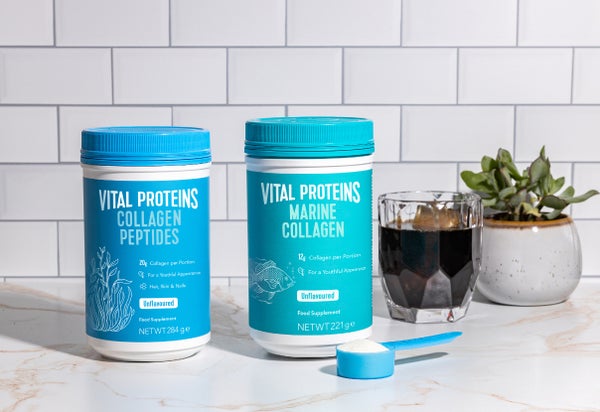 Vital Proteins Collagen Peptides and Marine Collagen Tins standing next to a cup of coffee.