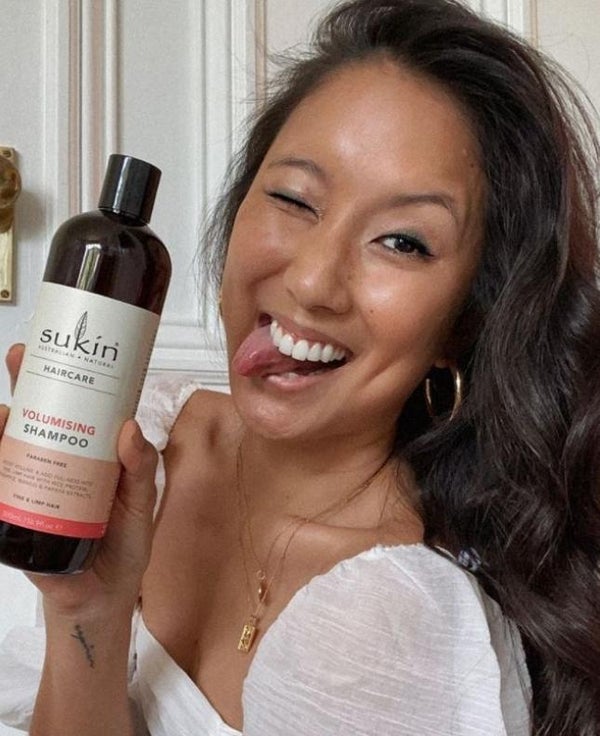 Girl smiling, holding Sukin Shampoo. Visit @SukinSkincare Instagram