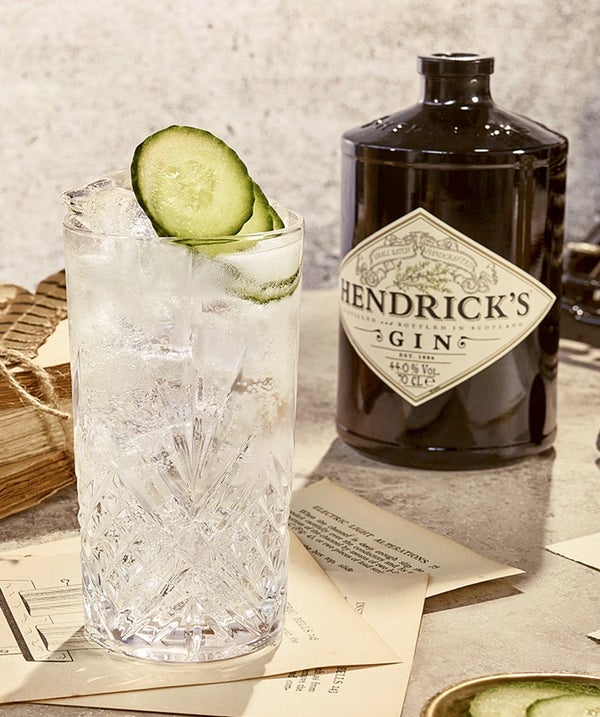 Hendrick's alcohol placed beside a cocktail in a glass, the cocktail contains ice and lime, there are sheets of paper scattered across the scene