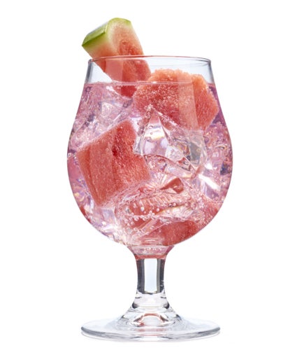 A cocktail containing ice, alcohol and watermelon chunks in a tall glass