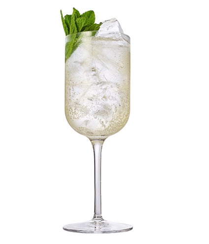 A glass with a tall stem containing a bubbly drink with ice and mint also present