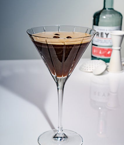 A cocktail in a glass with coffee beans on top of the drink